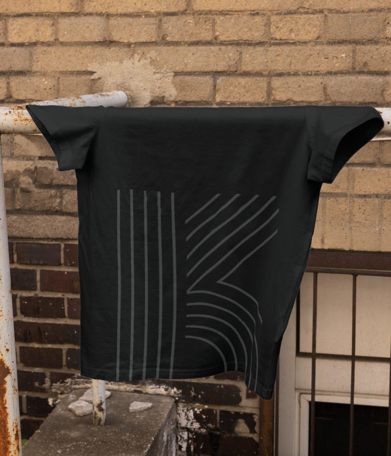 T-shirt Karborea noir suspendu devant un mur de brique